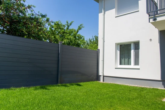 Scène extérieure résidentielle avec clôture moderne en aluminium noir à barreaux verticaux longeant une pelouse verte bien entretenue